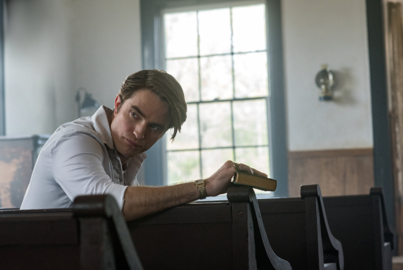 a man sitting at a desk in front of a window: Robert Pattinson in Netflix's The Devil All The Time