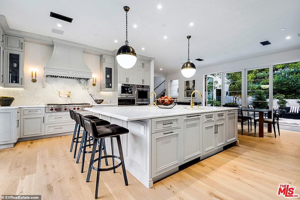 Center of attention: A large center island, with light grey cabinets and white marble counters takes center stage in the center of the room, with a gold plated sink and room for three barstools on a dining side
