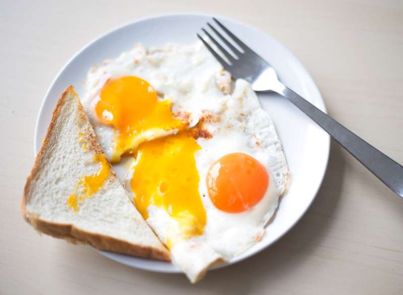 a plate of food with a fork and knife: Egg yolks will range in color—from pale yellow to deep orange to even a bright red—based on a hen's diet. Because free-range hens often eat more pigmented, nutritious foods that range from insects to grasses, eggs from these chickens often have richer-colored yolks. On the other hand, conventional, grain-fed chickens will produce lighter yellow yolks. As for those red yolks we mentioned? One chef—Dan Barber, executive chef of New York-based Blue Hill restaurants—worked with Cornell University researchers to develop a feed blend high in red peppers that allowed hens to produce strawberry-colored yolks.As for the difference in nutrients between yolk colors? The protein and fat counts will often remain the same regardless of yolk color, but there can be up to a 100-fold increase in micronutrient value of certain antioxidant carotenoids like lutein and beta-carotene in yolks fed a more nutrient-dense diet (like in pasture-raised hens), according to a 2010 study published in the Journal of the Science of Food and Agriculture. Rich, dark yolks will contain more of these potent antioxidants: compounds which mop up harmful toxins that promote inflammation and fat storage. Other studies have indicated that the same healthy diet that produces richer-colored yolks results in eggs with higher levels of heart-healthy omega-3s and less cholesterol.